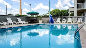 A swimming pool with lounge chairs and umbrellas, surrounded by a building with a balcony. - Quality Inn Moss Point - Pascagoula (Moss Point)