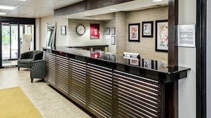 A reception area with a black reception desk, grey chairs, a clock, framed artwork, and a red emergency exit sign. - Quality Inn Moss Point - Pascagoula (Moss Point)