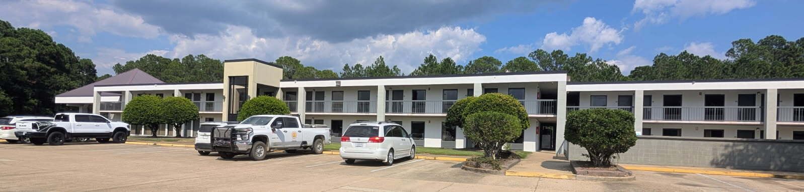 A motel with multiple two-story buildings, parking lot, and several vehicles parked.