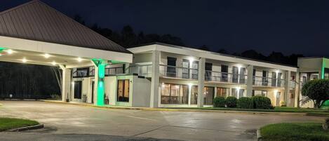 Un hotel de varios pisos con estacionamiento techado, iluminación exterior y un césped bien cuidado.