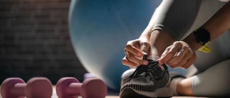A person tying shoelaces with dumbbells and a large exercise ball in the background.