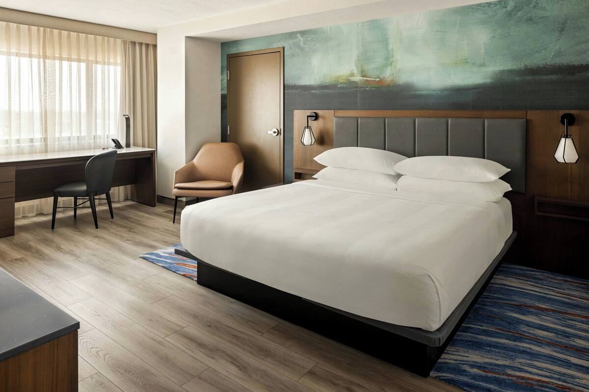 A hotel room with a large bed, a desk, a chair, and a painting on the wall.