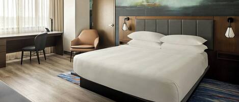 A hotel room with a large bed, a desk, a chair, and a painting on the wall.