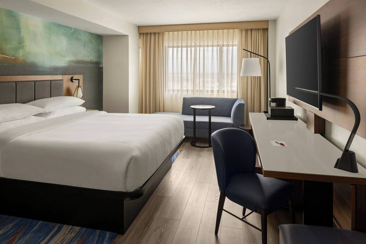 A hotel room with a large bed, a desk with a chair, a TV, and a window with curtains.
