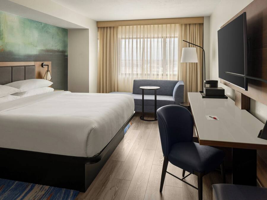 A hotel room with a large bed, a desk with a chair, a TV, and a window with curtains.