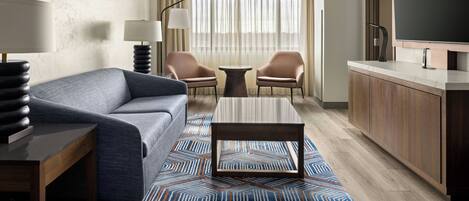 A hotel room with a sofa, two armchairs, a coffee table, a TV, and a minibar.