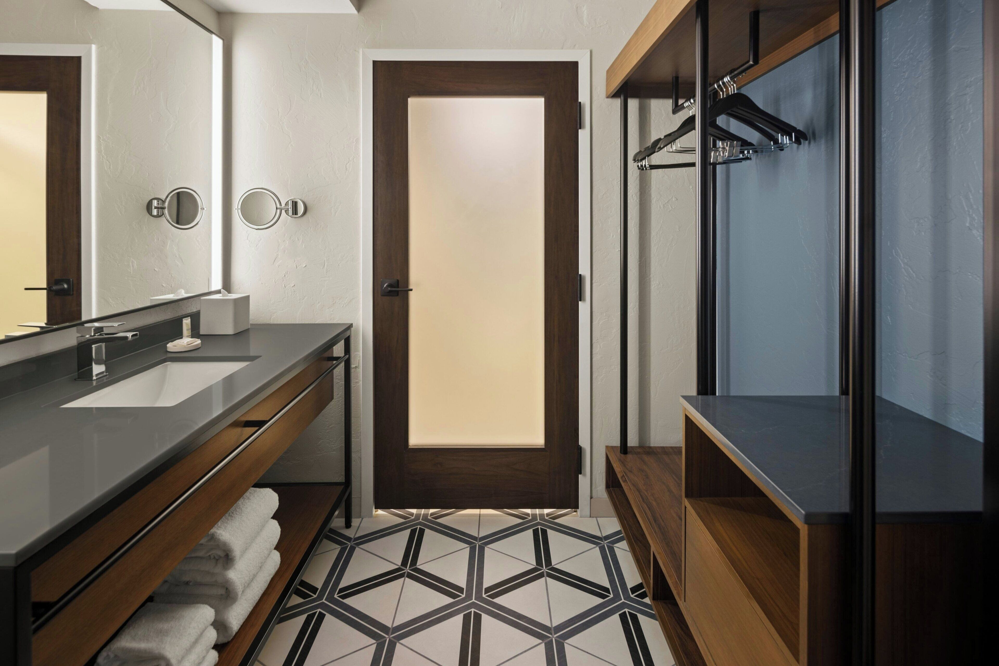 A modern bathroom with a double sink vanity, a mirror, a towel rack, and a shower area.