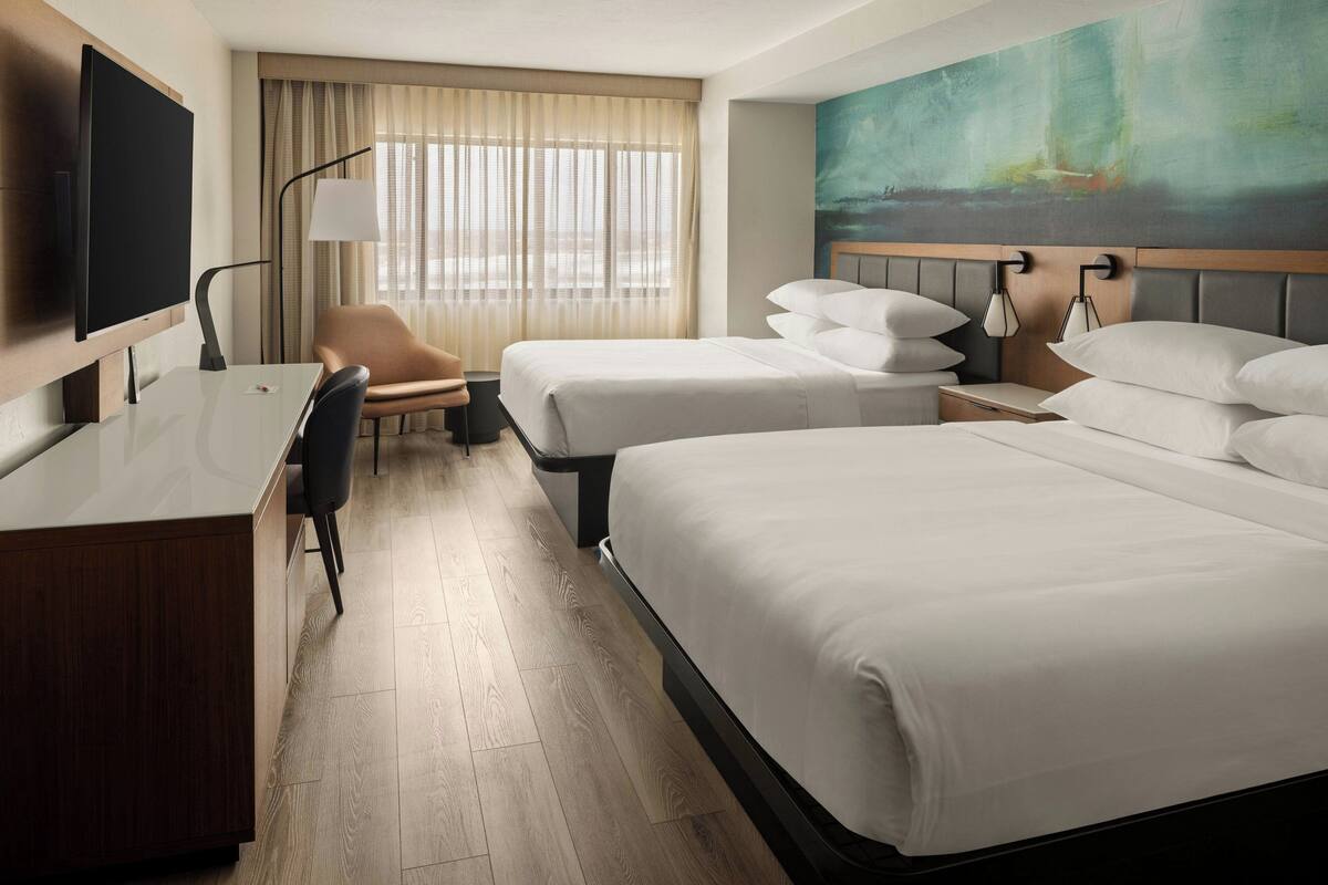 A hotel room with two beds, a desk, a chair, a TV, and a painting on the wall.