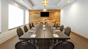 A conference room with a long table, chairs, a plant, and a TV on the wall.
