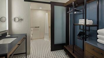 Un baño moderno con suelo de baldosas blanco y negro, un espejo grande, un tocador de madera y un vestidor con estantes para toallas.