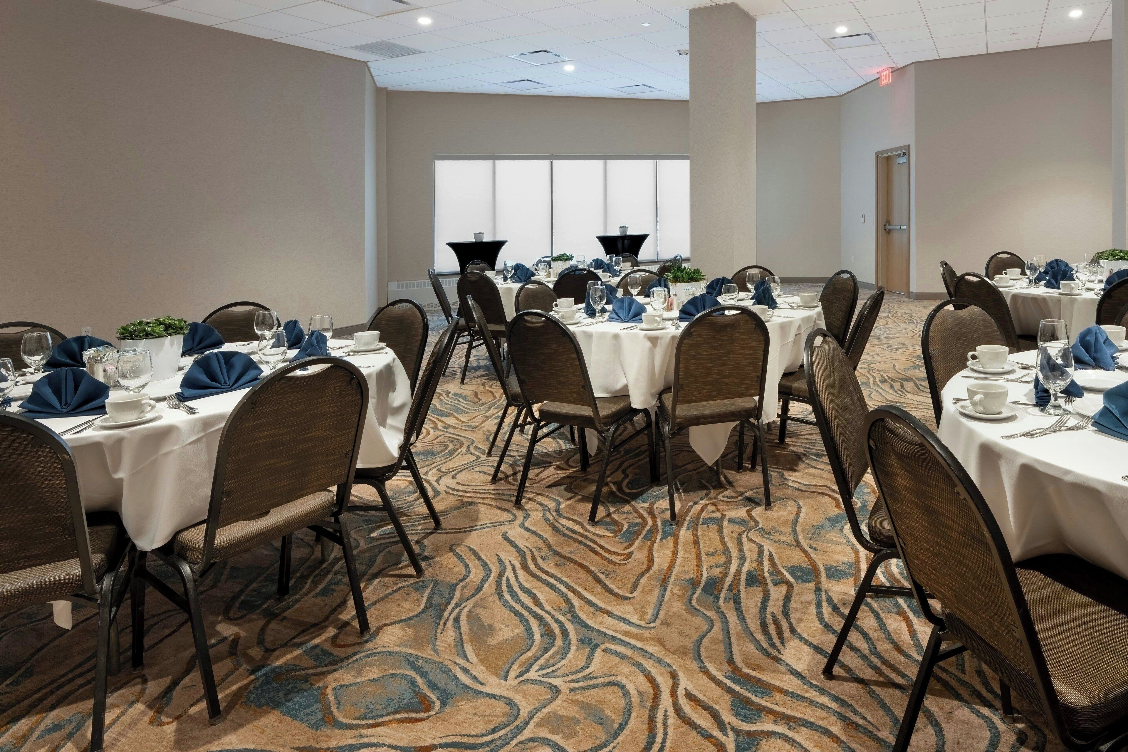 A conference room with multiple tables set for dining, equipped with chairs, tables, and centerpieces.