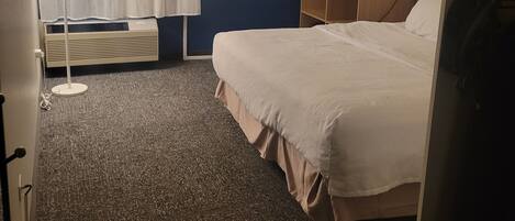 A hotel room with a bed, a desk, a lamp, a telephone, and a window with curtains.