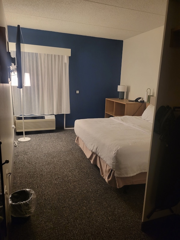 A hotel room with a bed, a desk, a lamp, a telephone, and a window with curtains.