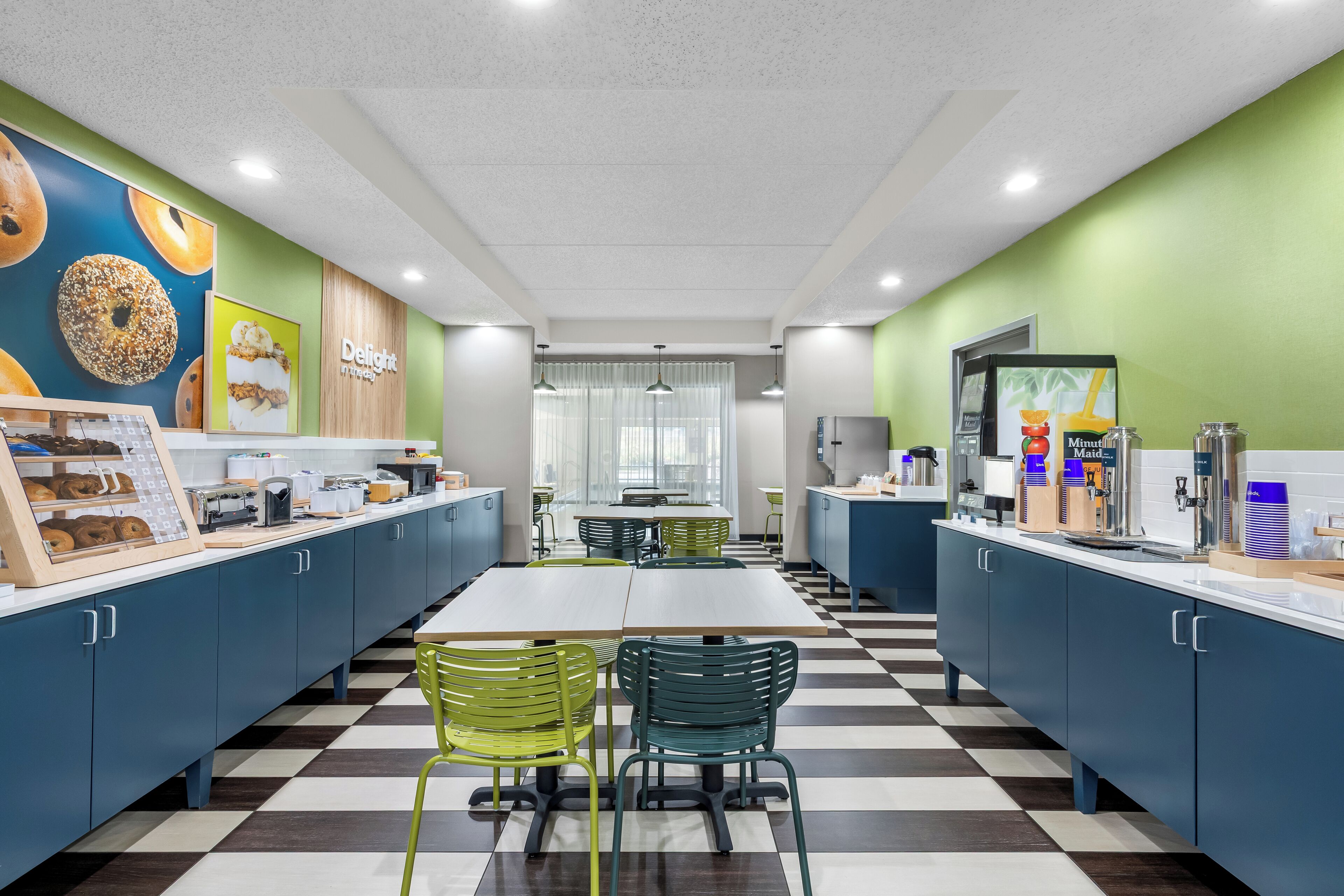 A modern café with a checkered floor, green and blue cabinets, and a counter with various food items and a coffee machine.