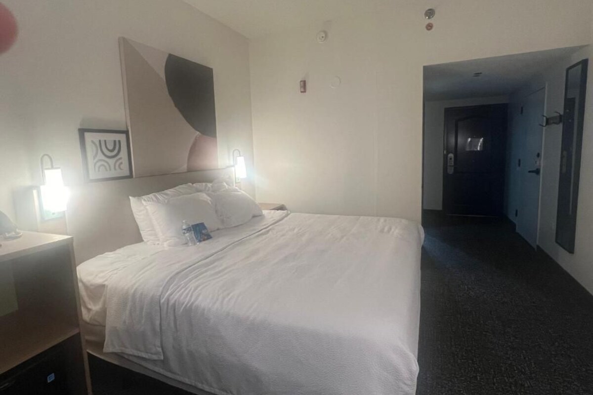 A hotel room with a large bed, bedside tables, a wall-mounted artwork, and a door leading to another room.
