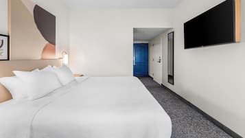 A hotel room with a large bed, a flat-screen TV mounted on the wall, and a door leading to another room.