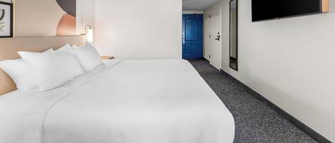 A hotel room with a large bed, a flat-screen TV mounted on the wall, and a door leading to another room.