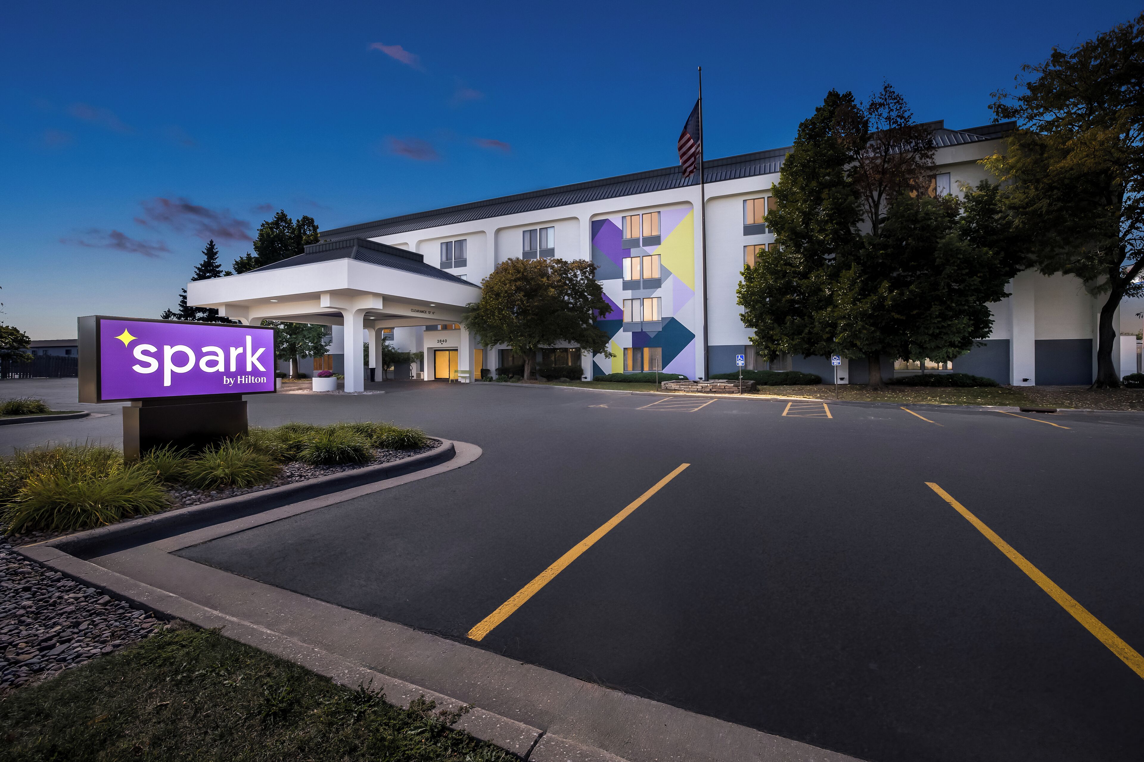 A hotel with a sign reading "spark by Hilton" and a parking lot with marked spaces.