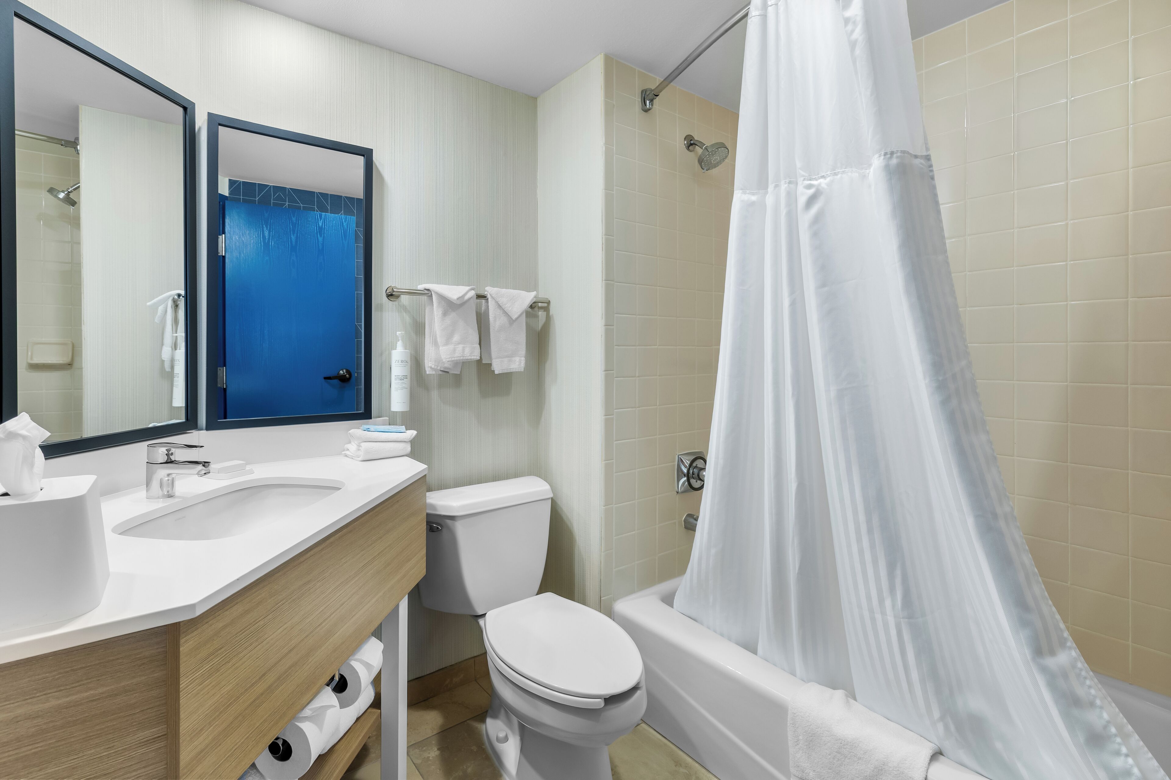 A modern bathroom with a white sink, toilet, and bathtub. There is a shower curtain, a towel rack with towels, and a mirror above the sink.