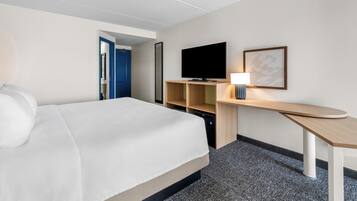 A hotel room with a bed, a television, a desk with a lamp, and a mirror on the wall.