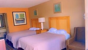 A hotel room with two beds, a nightstand with a lamp, and a chair. - Jax Inn (Jacksonville)
