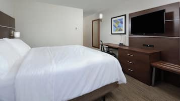 Habitación de hotel con una cama grande, un escritorio, una silla, un televisor de pantalla plana montado en la pared y un espejo.