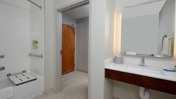 A modern bathroom with a white sink, a wooden vanity, a mirror, and a shower area.