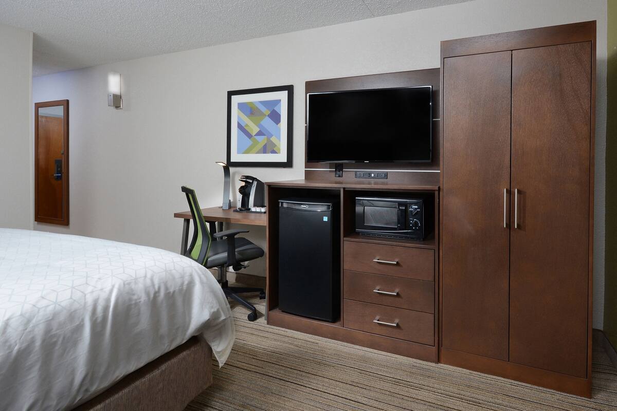 A hotel room with a bed, a desk with a computer, a television, a microwave, and a wardrobe.