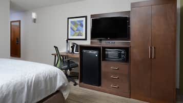 Une chambre d’hôtel équipée d’un lit, d’un bureau avec un ordinateur, d’une télévision, d’un four à micro-ondes et d’une armoire.