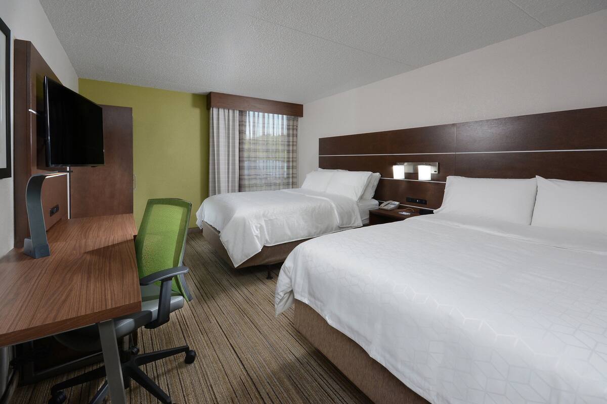 A hotel room with two beds, a desk, a chair, a television, and a window with curtains.