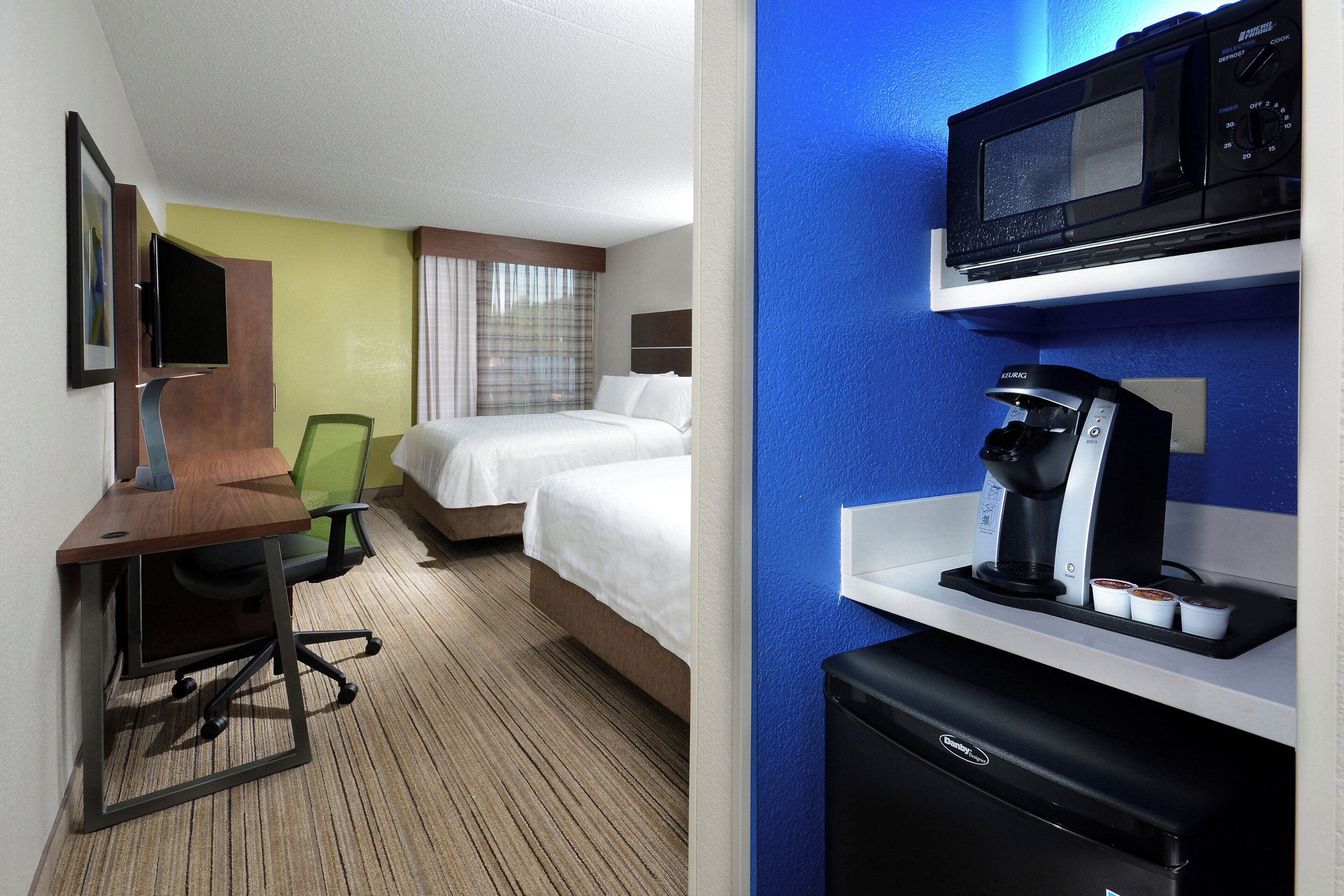 A hotel room with a desk, chair, two beds, a television, and a minibar.