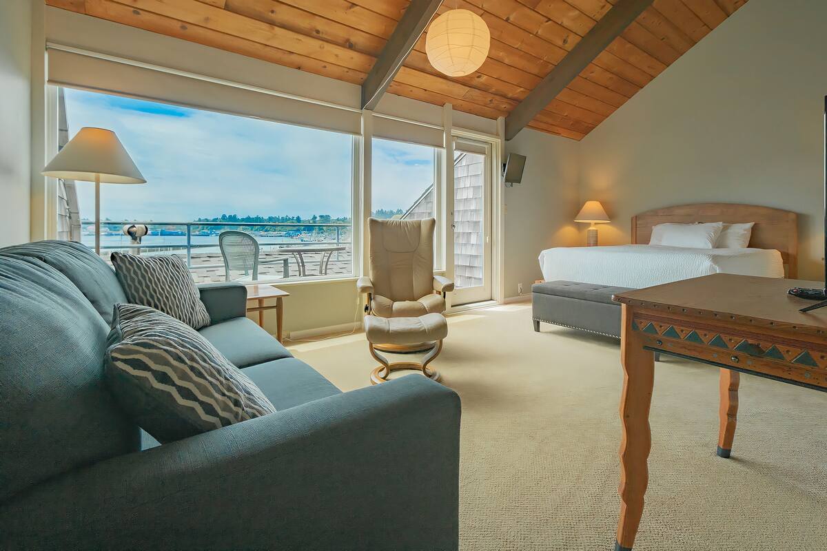 Una habitación de hotel con balcón, cama, sofá, sillón y mesa.
