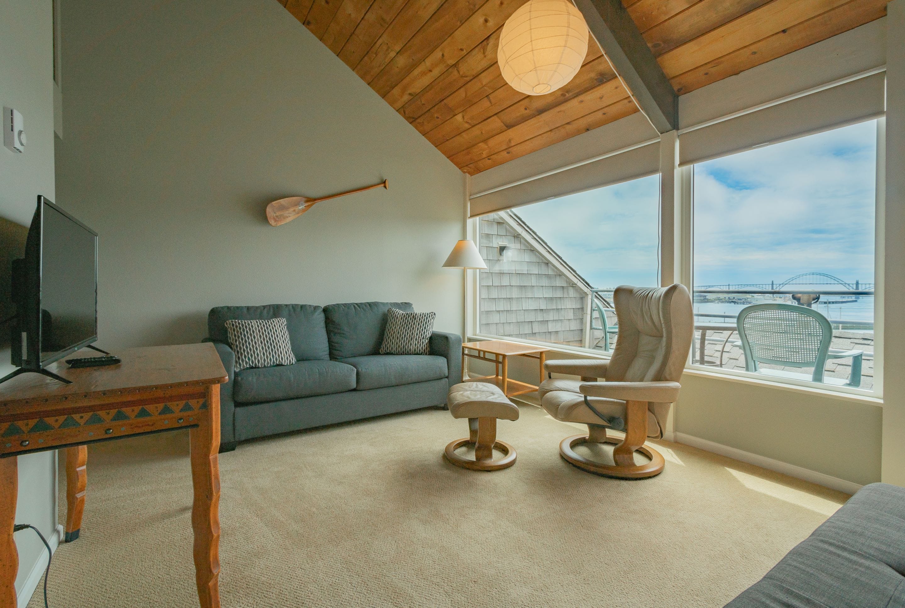 Una sala de estar acogedora con techo de madera, un sofá, una mesa de centro y vistas a un puente a través de amplias ventanas.