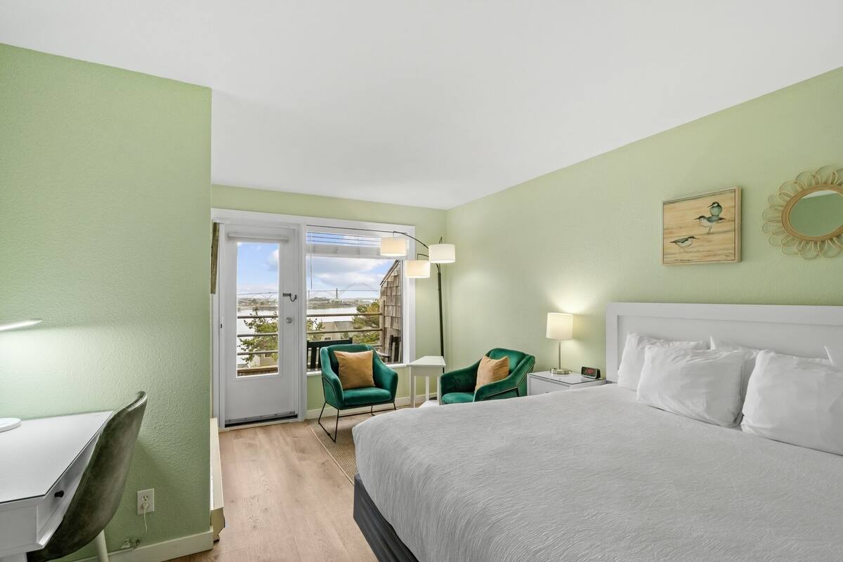 Habitación de hotel con cama, escritorio, silla y vistas al exterior.