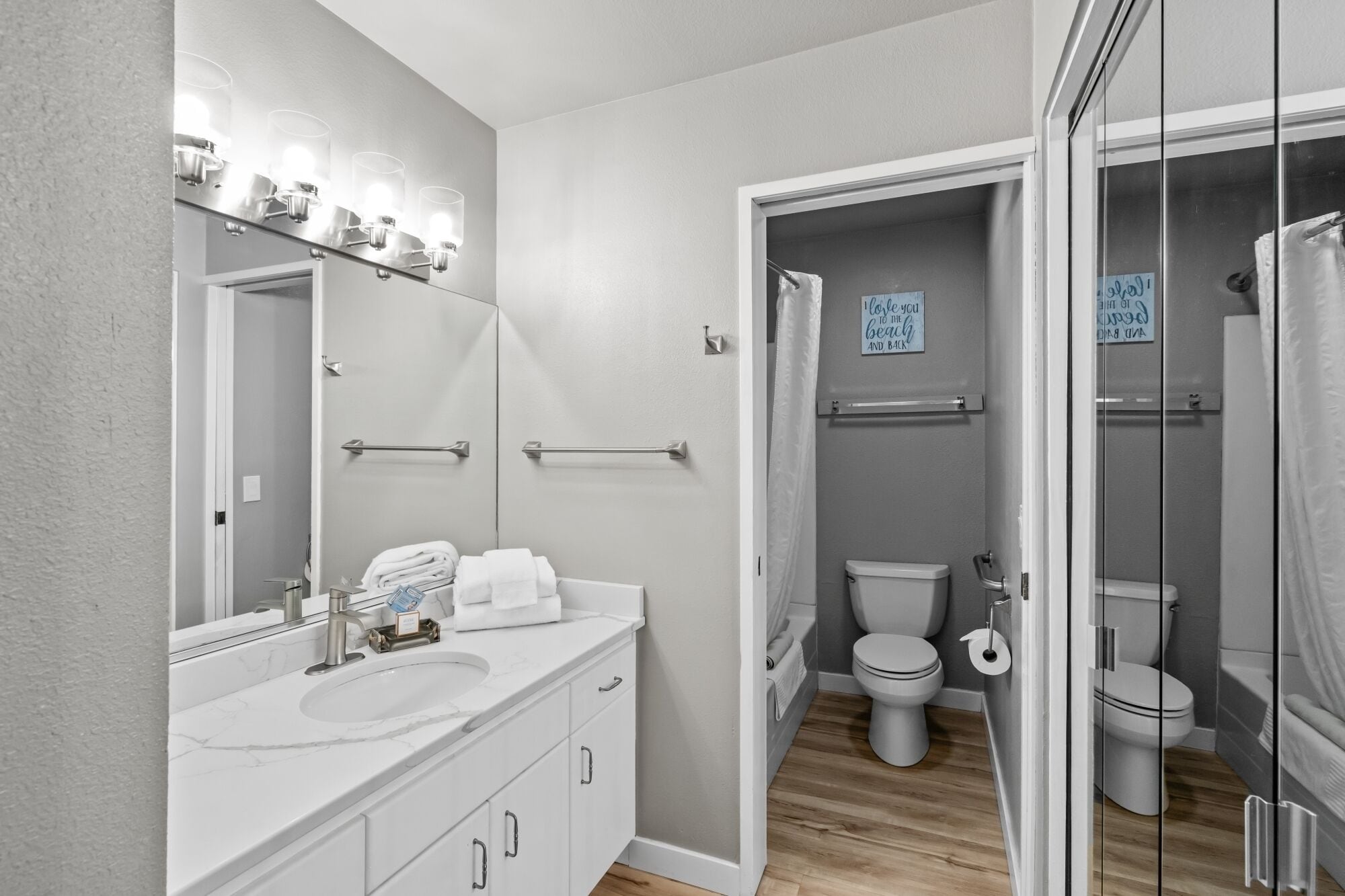 Un baño moderno con tocador blanco, un espejo grande y zona de ducha.