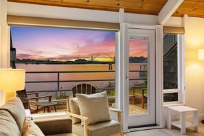 A room with a view of a sunset over a river, a sliding glass door, a sofa, a table, and a lamp. - Embarcadero Resort Hotel & Marina (Newport)