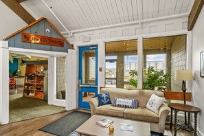 A cozy interior with a wooden ceiling, a blue door leading to a shop, a beige sofa with nautical-themed pillows, and a coffee table with magazines. - Embarcadero Resort Hotel & Marina (Newport)