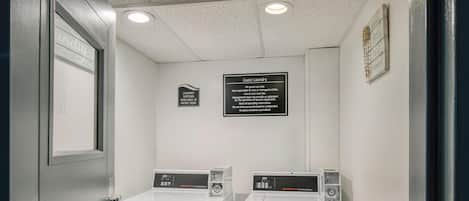A laundry area with two front-loading washers and dryers, a sign indicating guest laundry rules, and a calendar on the wall.