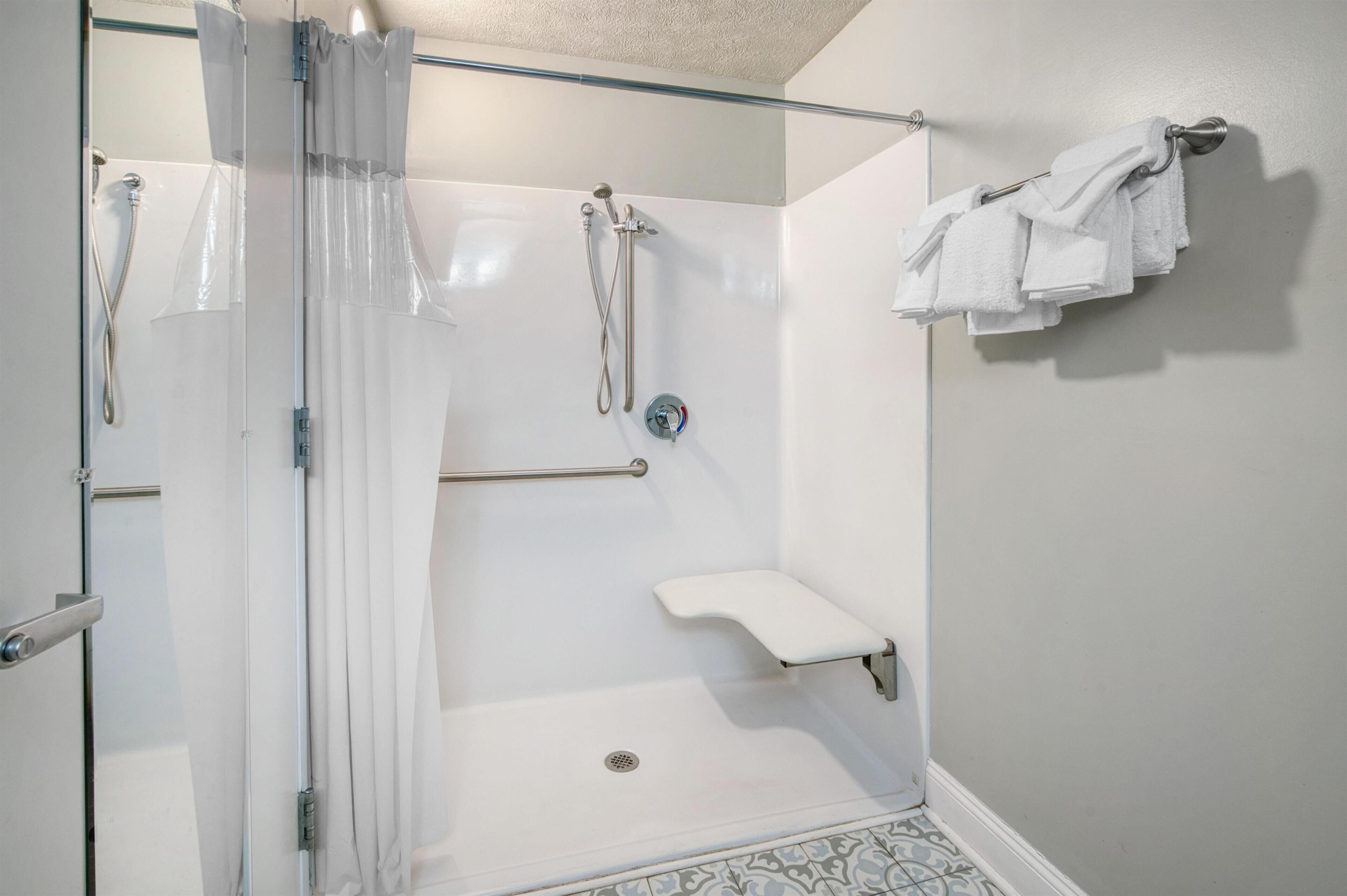 Une douche avec une porte en verre, une barre d’appui, un porte-serviettes et une petite étagère.