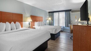 A hotel room with two beds, a desk, a chair, and a television.
