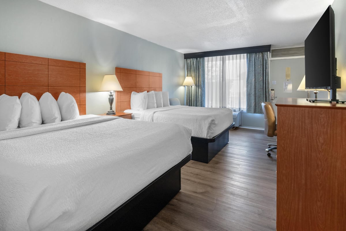 A hotel room with two beds, a desk, a chair, and a television.