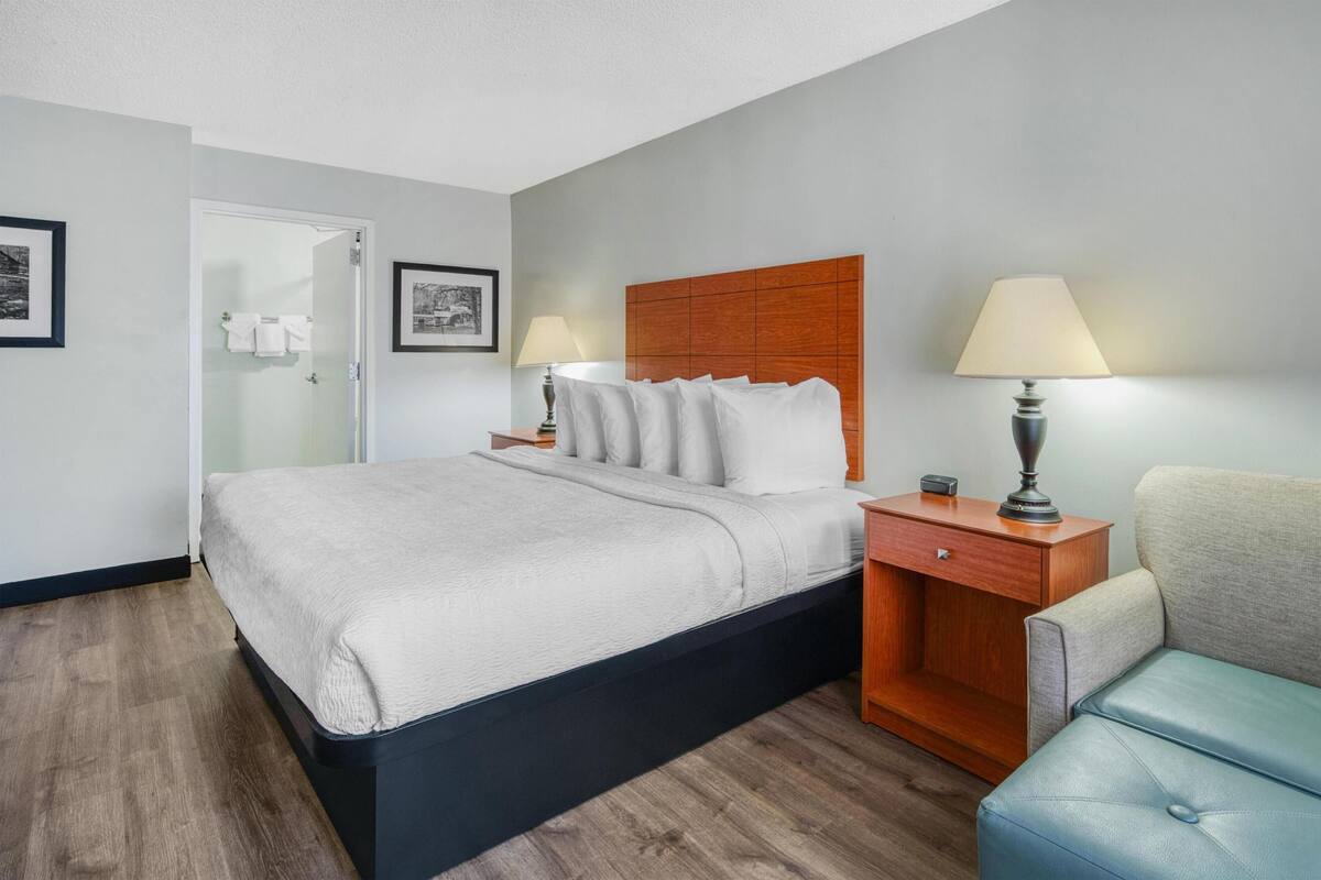 A hotel room with a bed, bedside tables, a chair, and a wooden headboard.