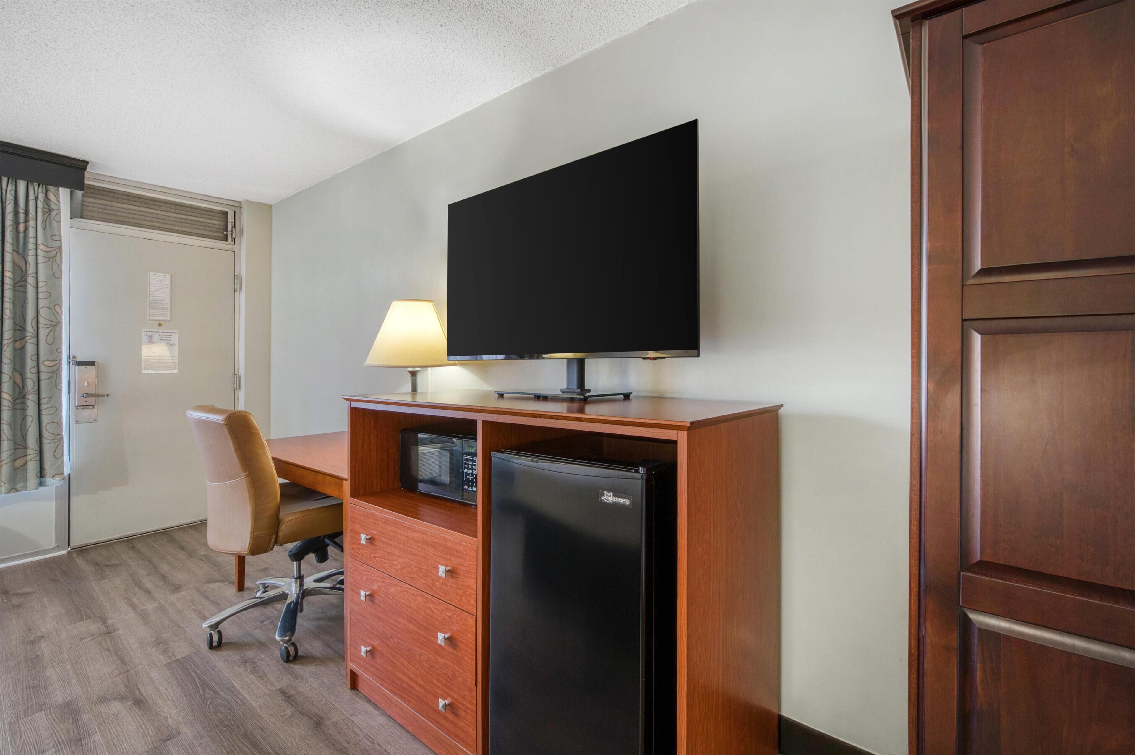 Habitación de hotel con un escritorio de madera, televisión, refrigerador, una silla y una lámpara.