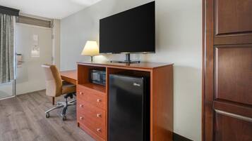 Habitación de hotel con un escritorio de madera, televisión, refrigerador, una silla y una lámpara.