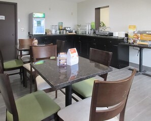 A hotel dining area with a marble table, green cushioned chairs, and a breakfast bar with a sign for pancakes.