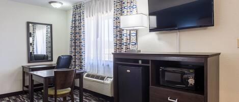 Habitación de hotel con escritorio, silla, televisor, microondas y refrigerador.