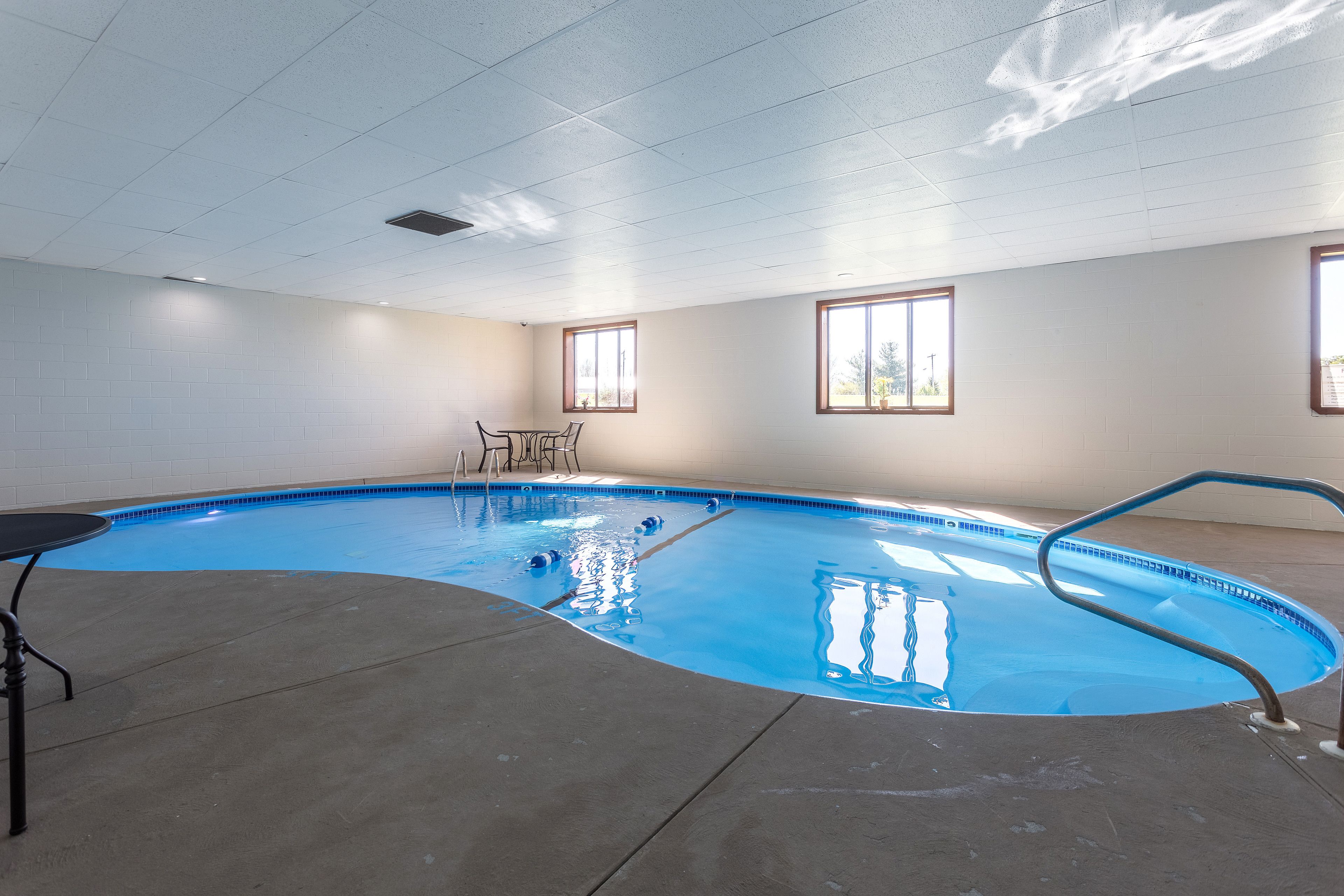 An indoor swimming pool with a clear view of the ceiling, windows, and a table with chairs.