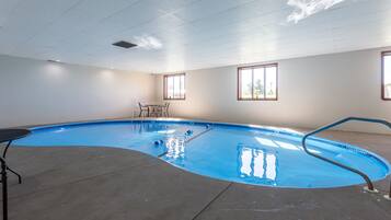 An indoor swimming pool with a clear view of the ceiling, windows, and a table with chairs.