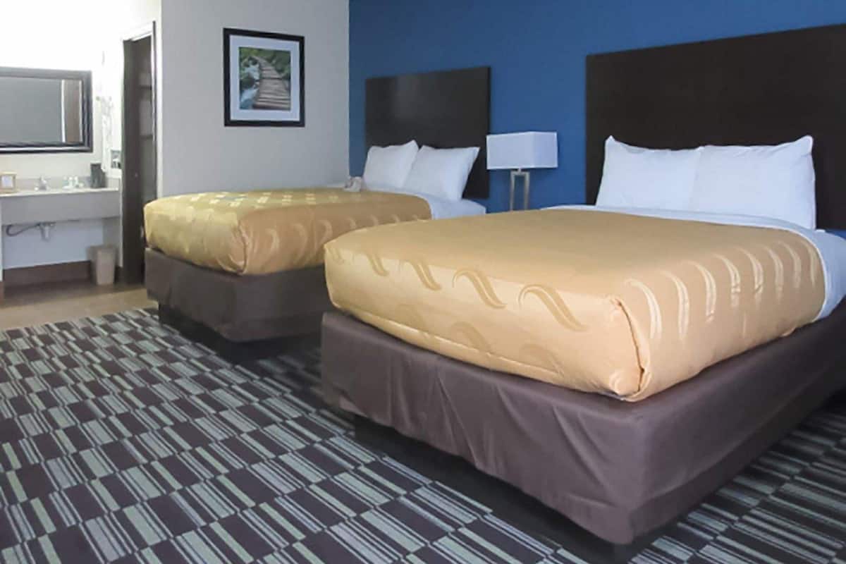 A hotel room with two beds, a bathroom, and a large window.