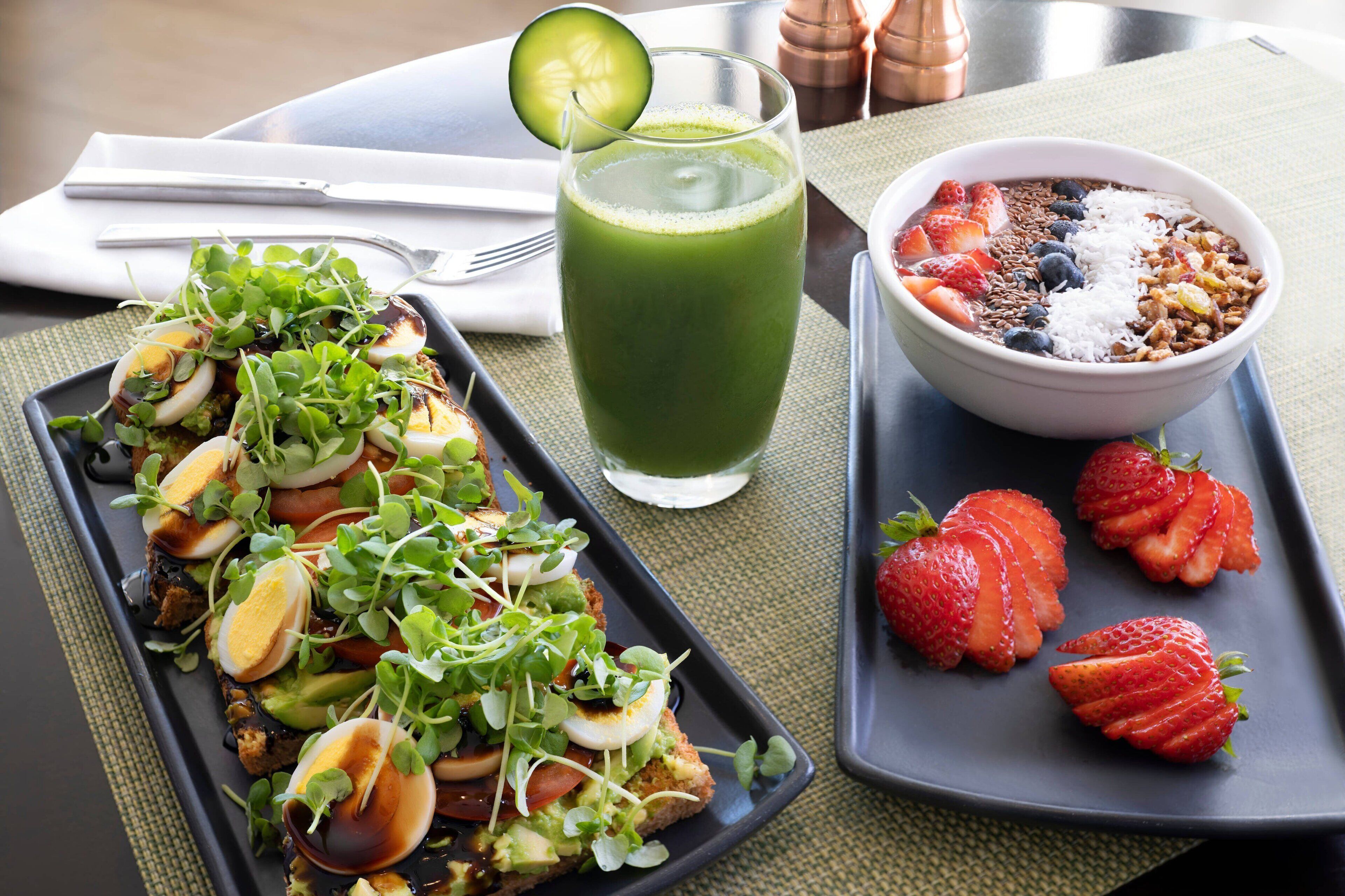 A meal with a green smoothie, a bowl of granola with fruits, and a plate with a salad and sliced strawberries.